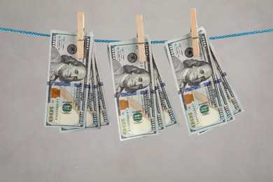 Dollar banknotes hanging on rope against light grey background