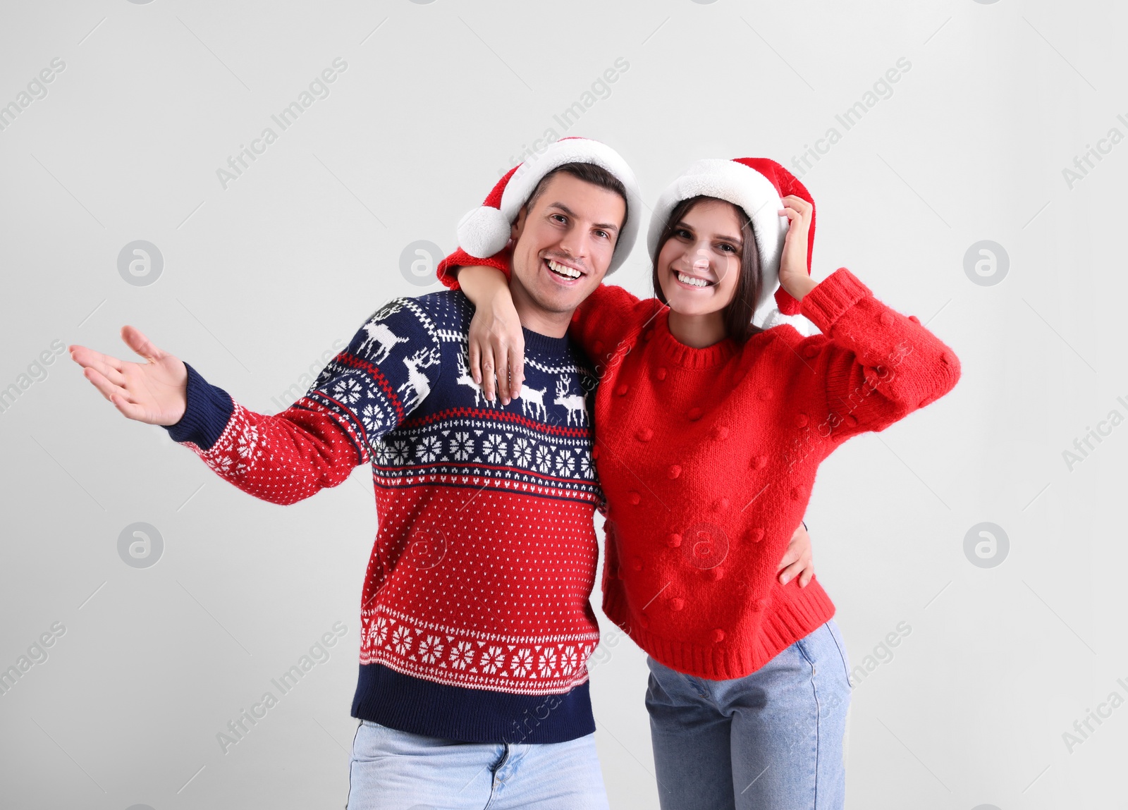 Photo of Beautiful happy couple in Santa hats and Christmas sweaters having fun on light background