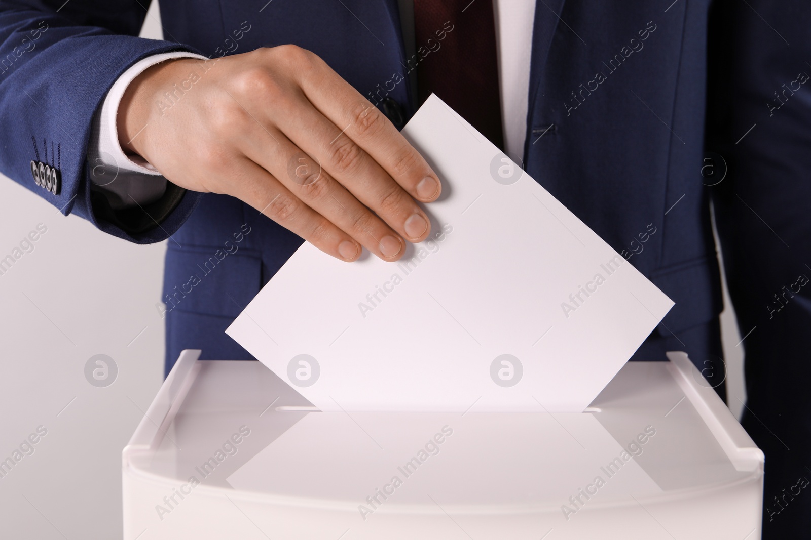 Photo of Man putting his vote into ballot box on light grey background, closeup