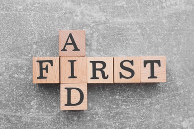 Photo of Words First Aid made of wooden cubes on light grey table, top view