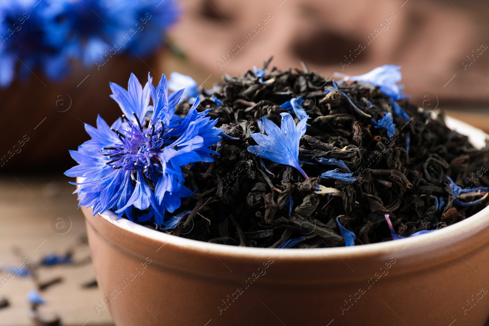 Photo of Bowl with dry tea leaves and cornflower, closeup