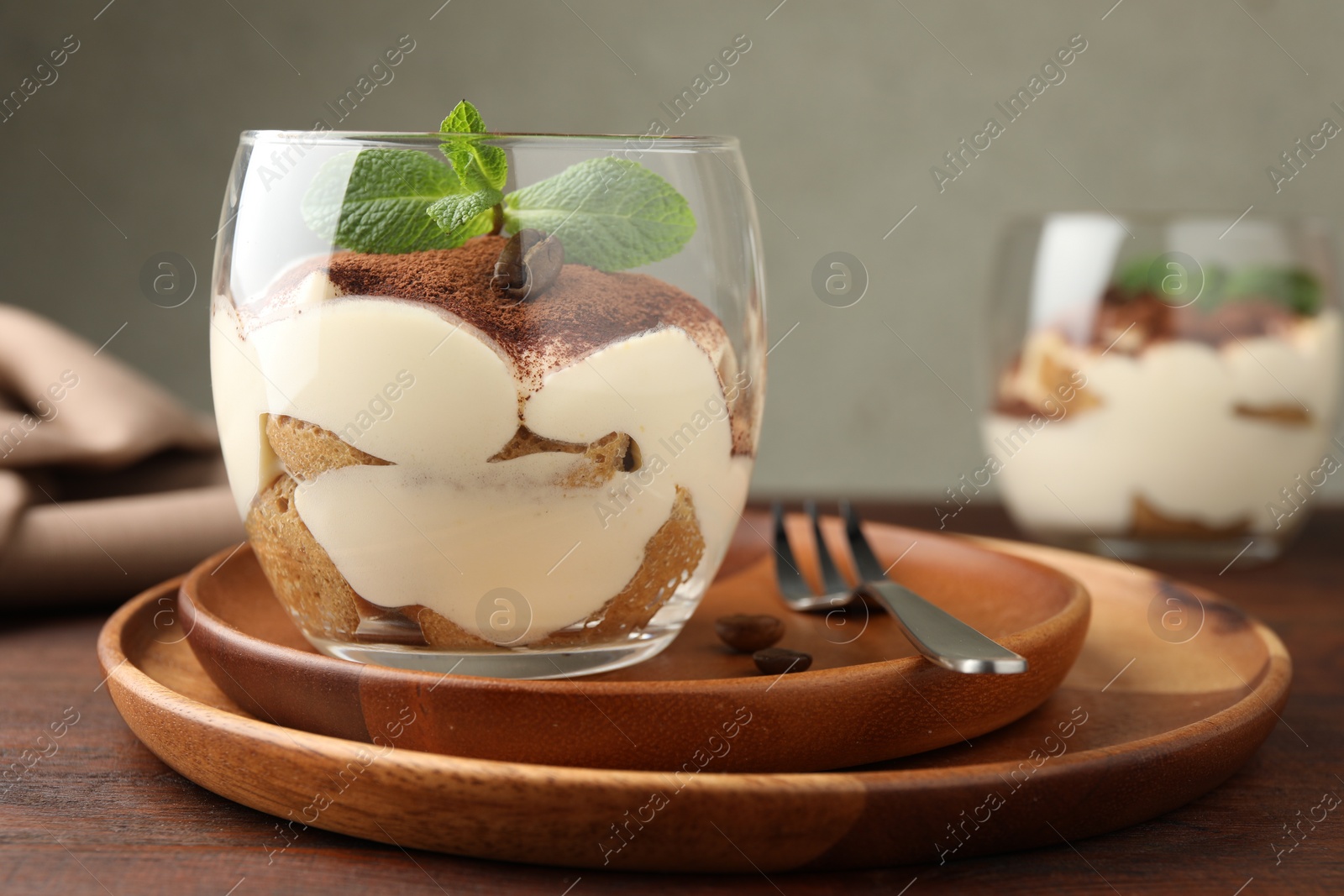 Photo of Delicious tiramisu in glass, mint leaves, coffee beans and fork on wooden table, closeup