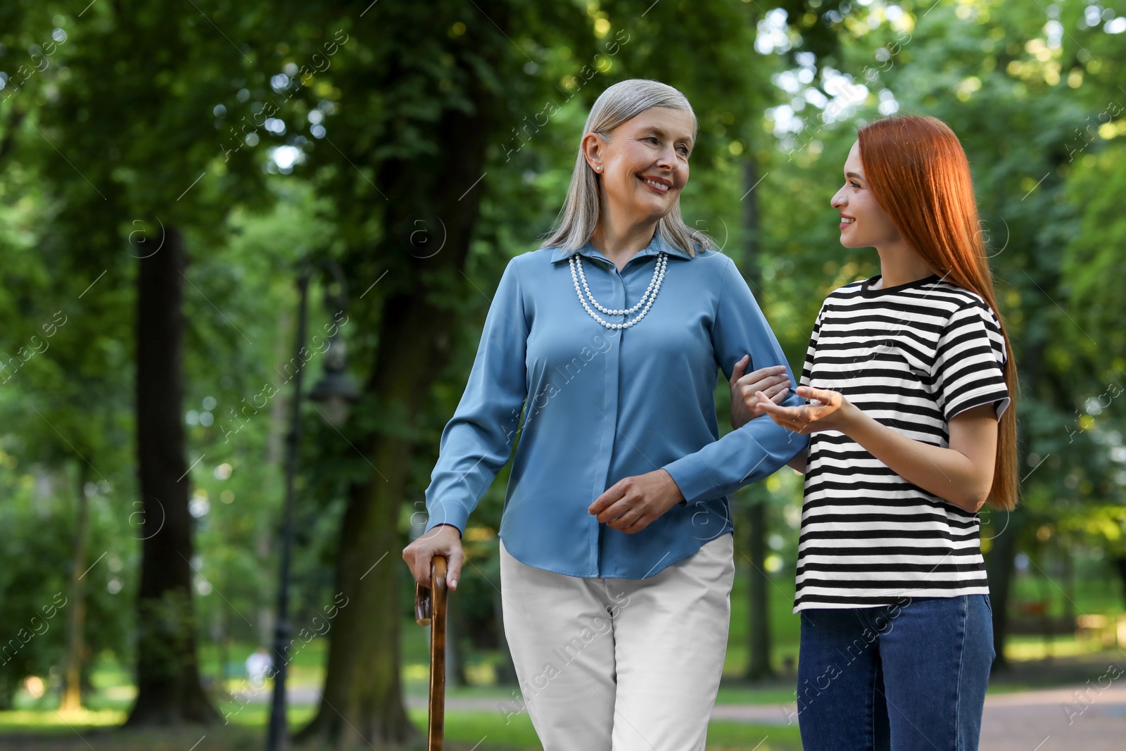 Photo of Senior lady with walking cane and young woman in park. Space for text