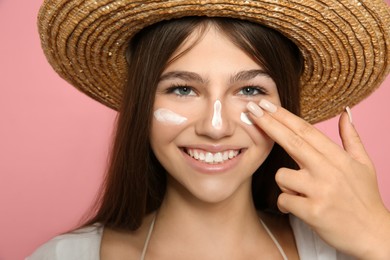 Photo of Teenage girl applying sun protection cream on her face against pink background