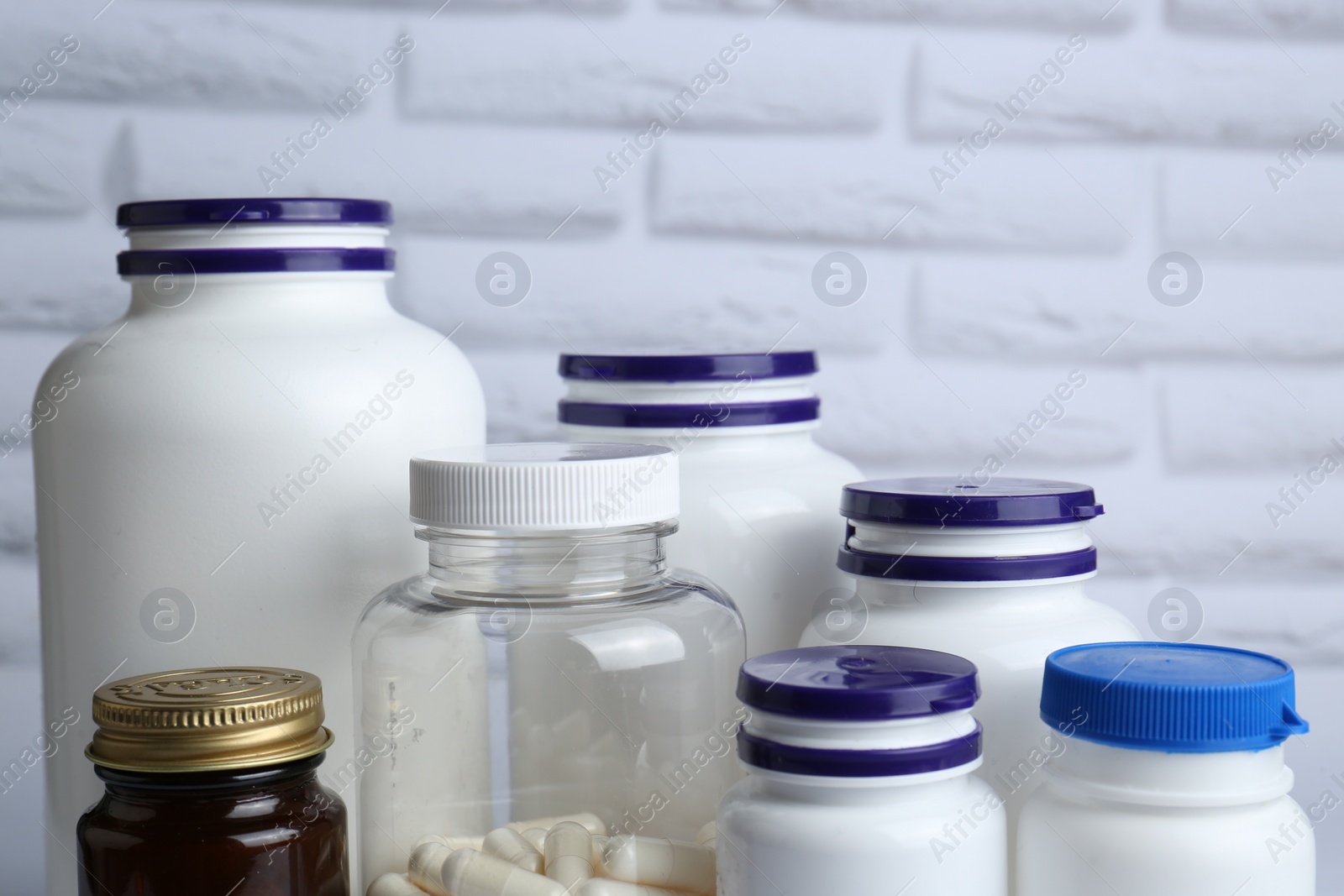 Photo of Different medical bottles near white brick wall, closeup