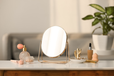 Photo of Mirror, jewelry and makeup products on white table indoors