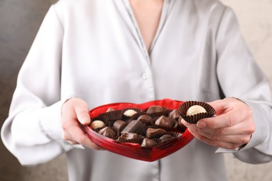 Woman holding heart shaped box with delicious chocolate candies, closeup