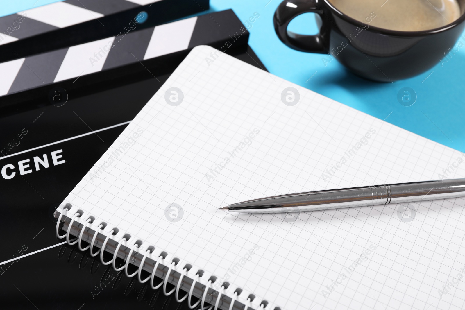 Photo of Movie clapper, coffee, notebook and pen on light blue table