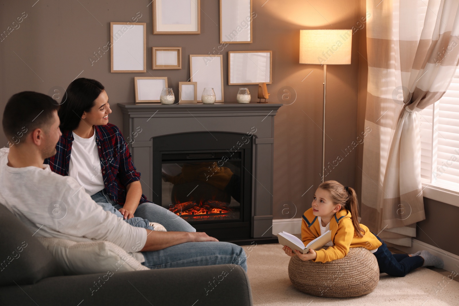 Photo of Happy family reading book together near fireplace at home