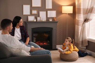 Photo of Happy family reading book together near fireplace at home