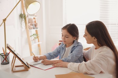 Mother helping her daughter with homework using tablet at home