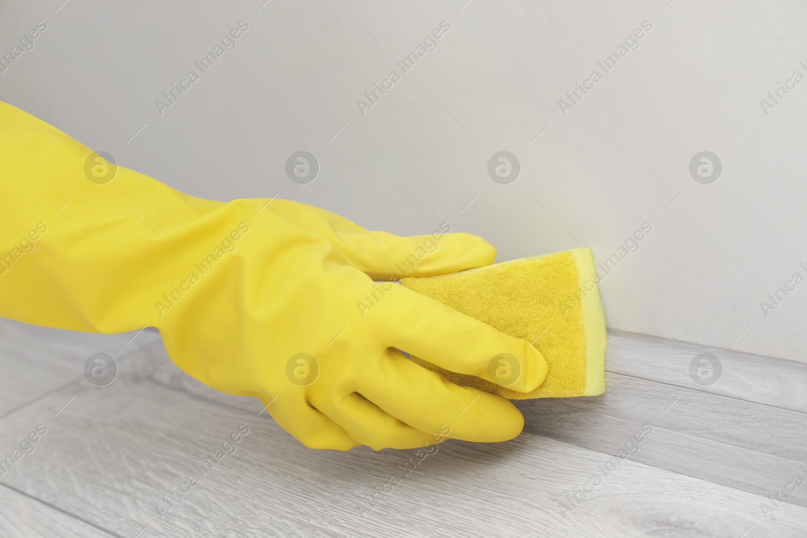 Photo of Woman in protective glove cleaning plinth with sponge indoors, closeup