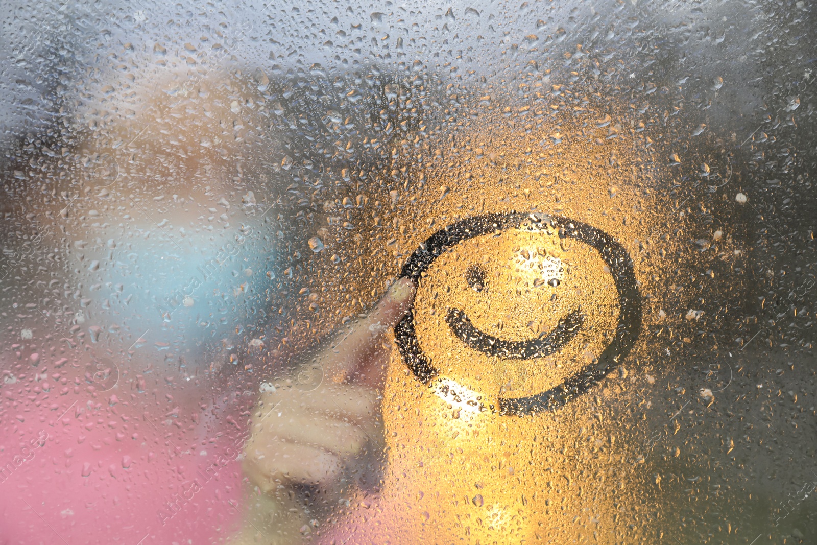 Photo of Woman drawing happy face on foggy window at rainy weather, closeup
