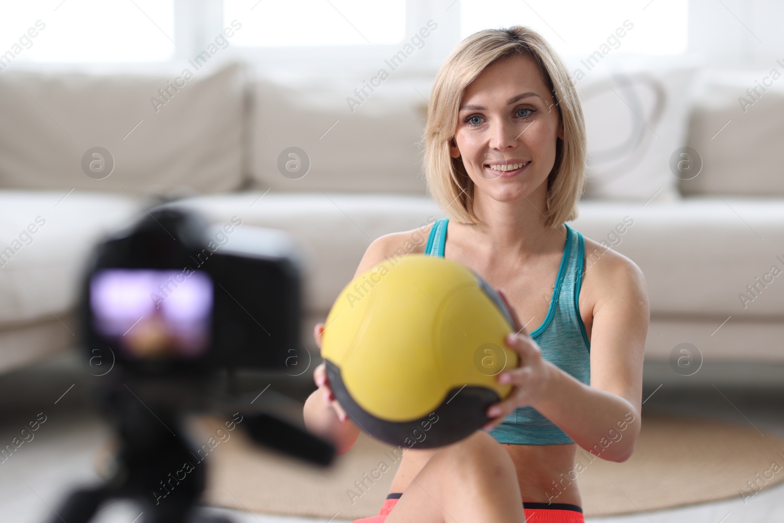 Photo of Smiling sports blogger holding medicine ball while recording fitness lesson with camera at home