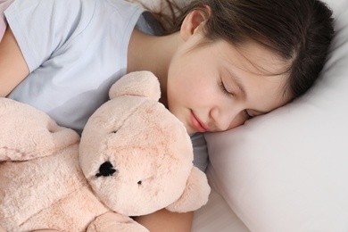 Beautiful little girl with teddy bear sleeping in bed