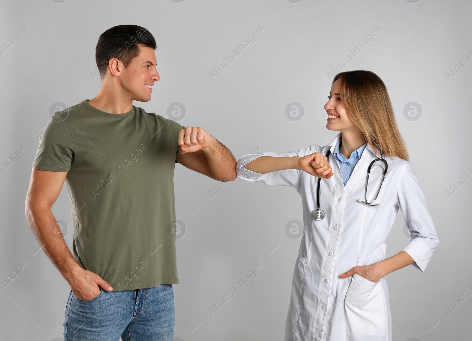 Photo of Doctor and patient doing elbow bump instead of handshake on light grey background. New greeting during COVID-19 pandemic