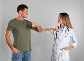 Photo of Doctor and patient doing elbow bump instead of handshake on light grey background. New greeting during COVID-19 pandemic