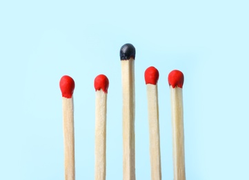 Photo of Row of whole matches and burnt one on light blue background. Uniqueness concept