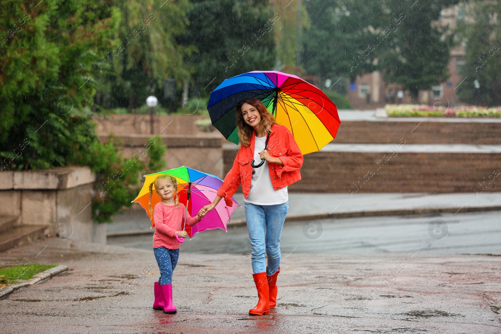 Photo of Happy mother and daughter with bright umbrella under rain outdoors