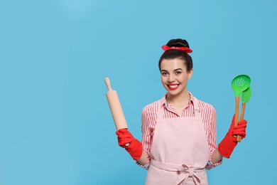 Photo of Young housewife with cooking utensils on light blue background, space for text