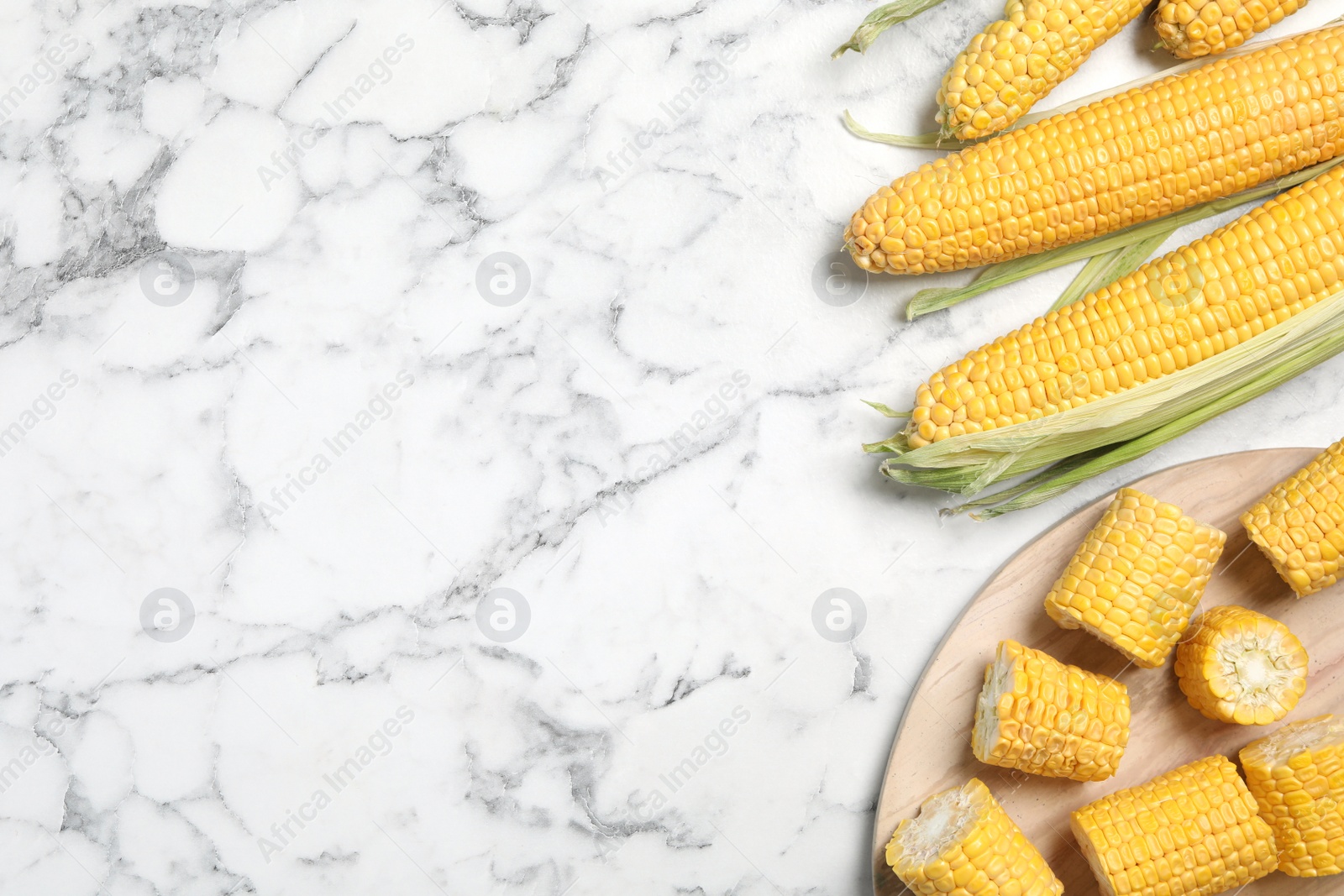 Photo of Bunch of corn cobs on white marble table, flat lay. Space for text