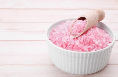 Photo of Bowl and scoop with pink sea salt on white wooden table, closeup. Space for text