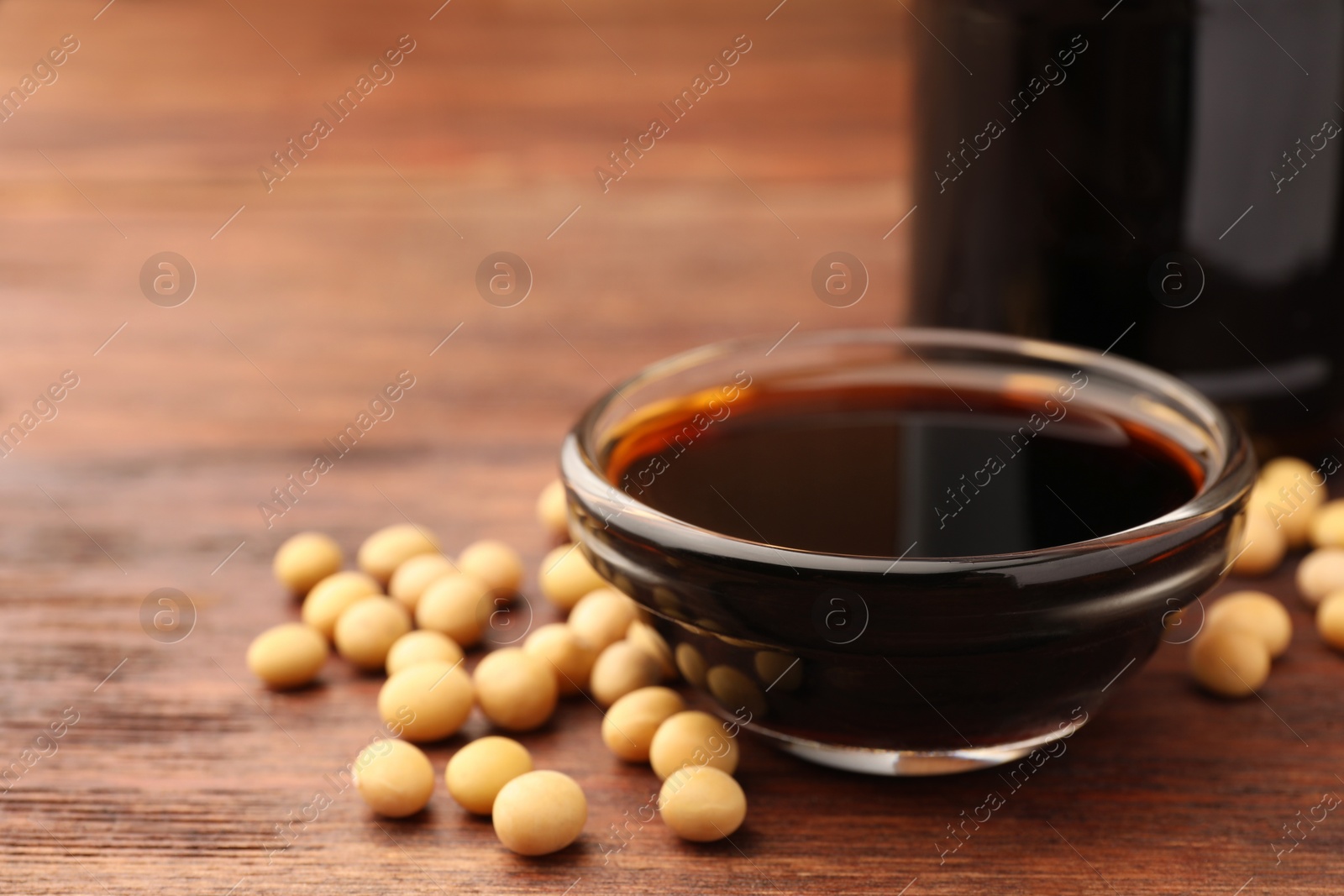 Photo of Soy sauce in bowl and soybeans on wooden table, closeup