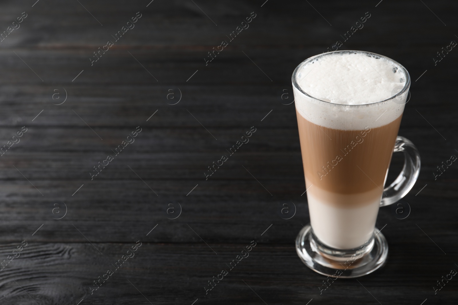 Photo of Glass cup of delicious layered coffee on black wooden table, space for text