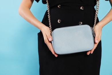 Woman with stylish bag on light blue background, closeup