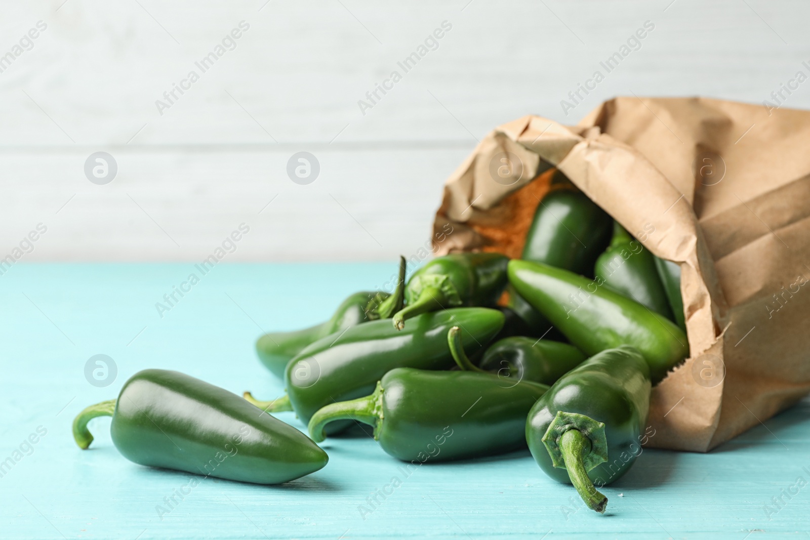 Photo of Paper bag with green hot chili peppers on light blue wooden table. Space for text