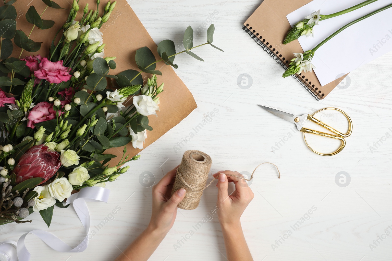 Photo of Florist making beautiful bouquet at white wooden table, top view