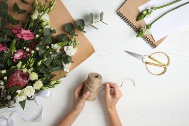 Photo of Florist making beautiful bouquet at white wooden table, top view