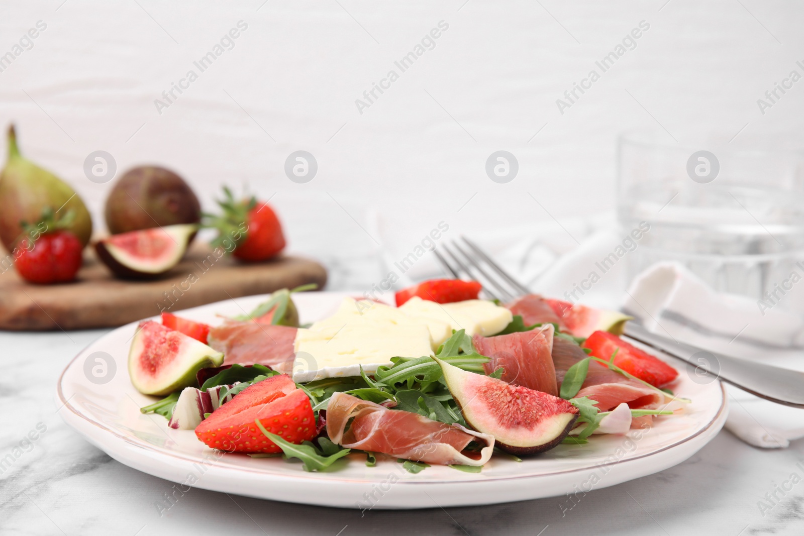 Photo of Tasty salad with brie cheese, prosciutto, strawberries and figs on white marble table