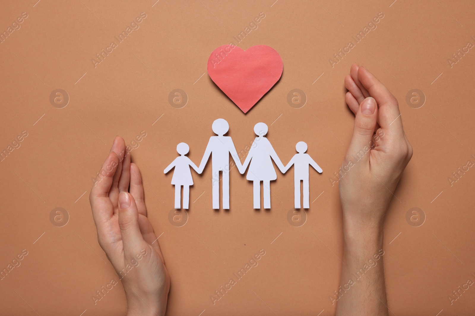 Photo of Woman protecting paper family figures and red heart on brown background, top view. Insurance concept