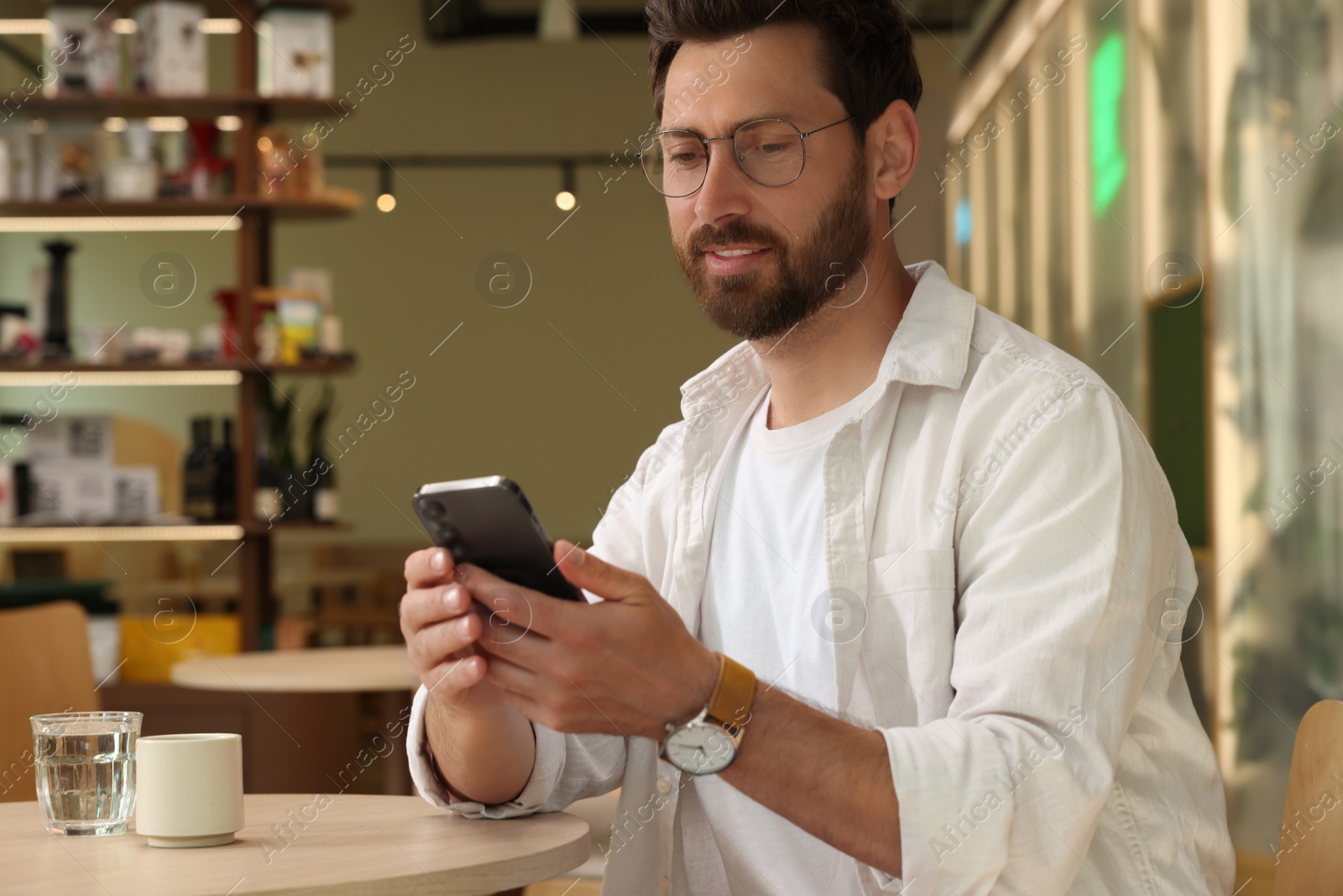 Photo of Handsome man using smartphone at table in cafe