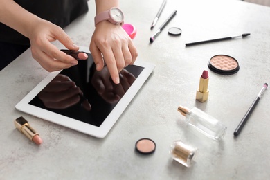 Photo of Young woman with makeup products using tablet at table. Beauty blogger