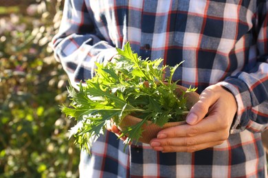 Woman holding wooden bowl with fresh mizuna leaves outdoors, closeup