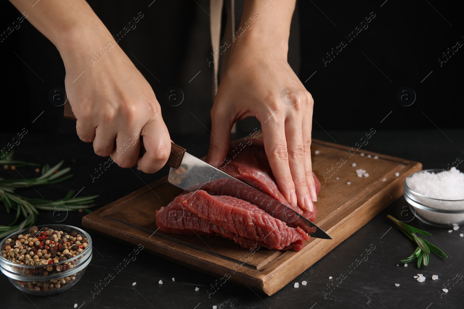 Photo of Woman cutting fresh raw meat at black table, closeup