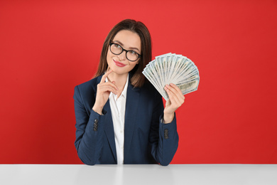 Young woman with money at table on crimson background