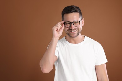 Photo of Portrait of happy man in stylish glasses on brown background. Space for text