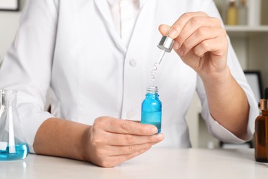 Photo of Dermatologist developing cosmetic product at white table indoors, closeup