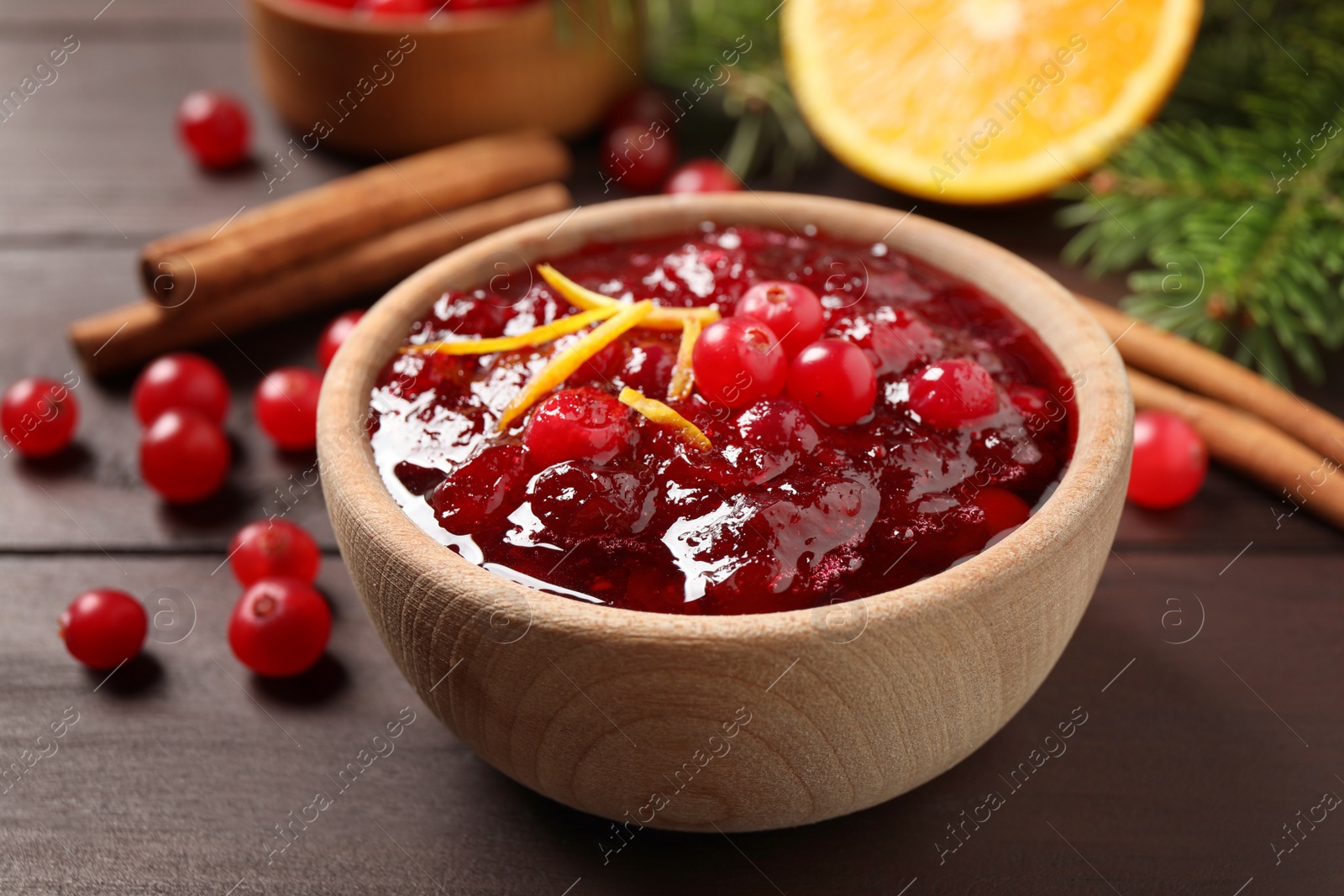 Photo of Cranberry sauce with orange peel on wooden table, closeup