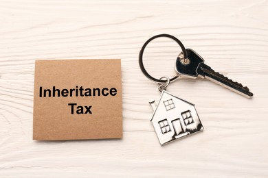 Photo of Inheritance Tax. Card and key with metallic key chain in shape of house on white wooden table, flat lay