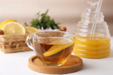 Cup of delicious tea with lemon and honey on white table, closeup