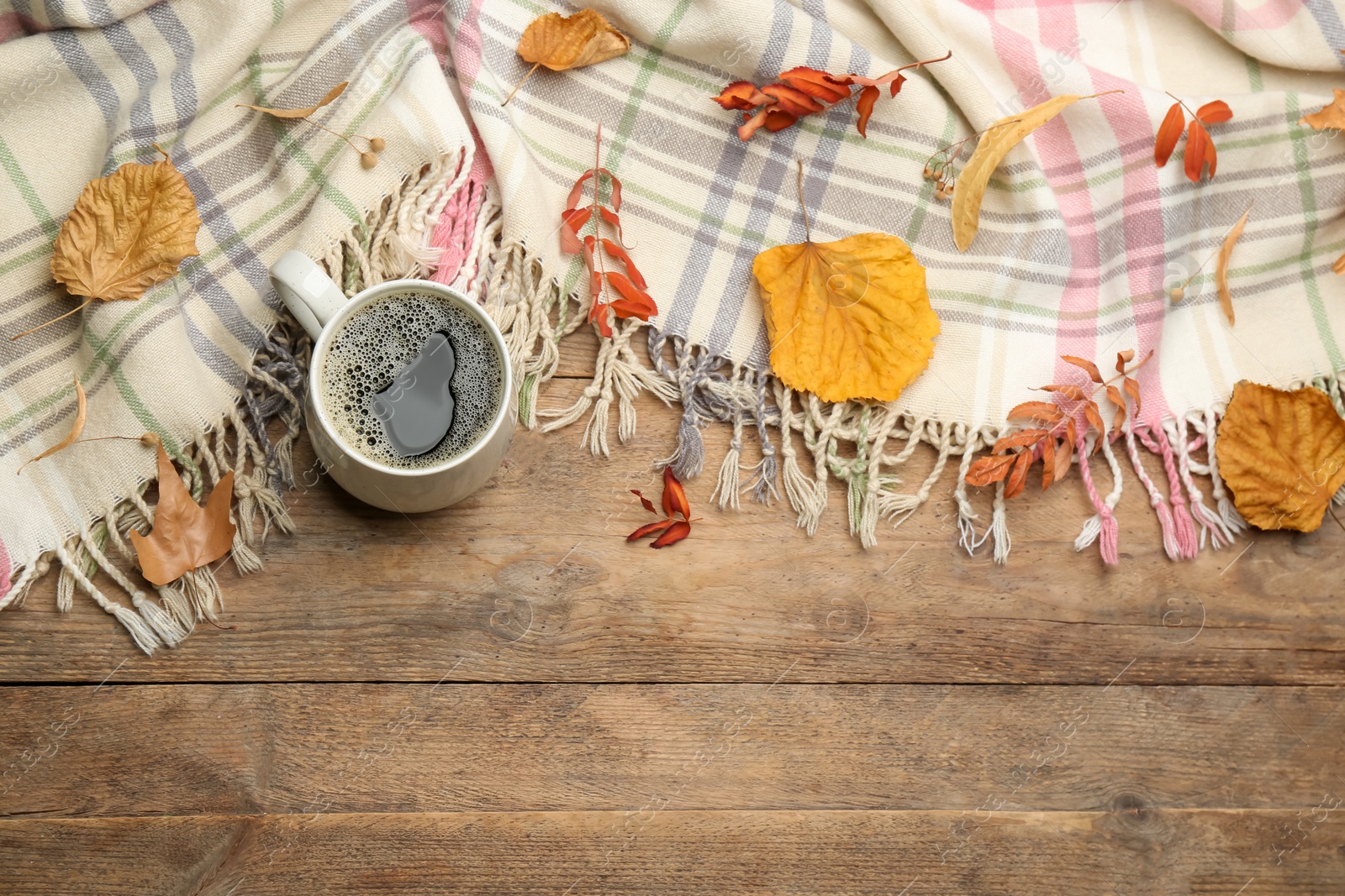 Photo of Composition with hot drink and warm plaid on wooden table, above view. Space for text