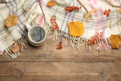 Composition with hot drink and warm plaid on wooden table, above view. Space for text