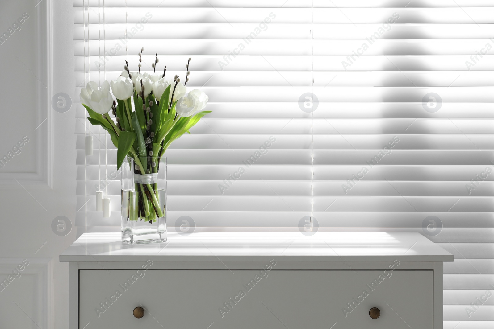 Photo of Beautiful bouquet of willow branches and tulips in vase near window indoors, space for text