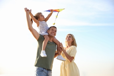 Photo of Happy parents with their child playing with kite on beach. Spending time in nature