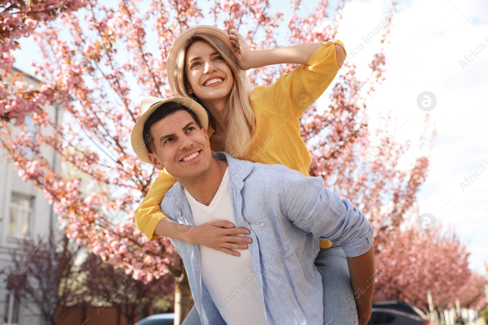 Photo of Happy stylish couple near blossoming sakura tree on city street. Spring family look