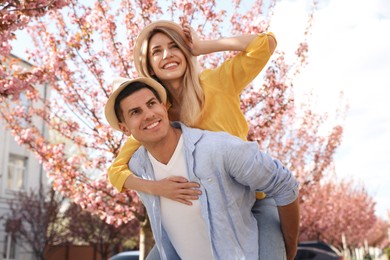 Photo of Happy stylish couple near blossoming sakura tree on city street. Spring family look